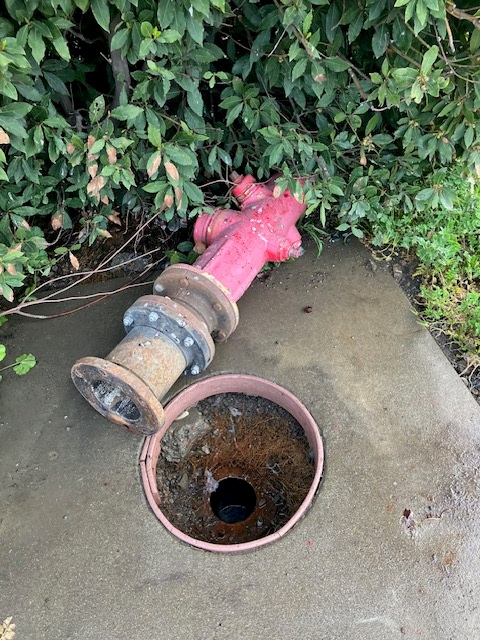 Damaged private fire hydrant with exposed rusted piping and open valve box needing repair