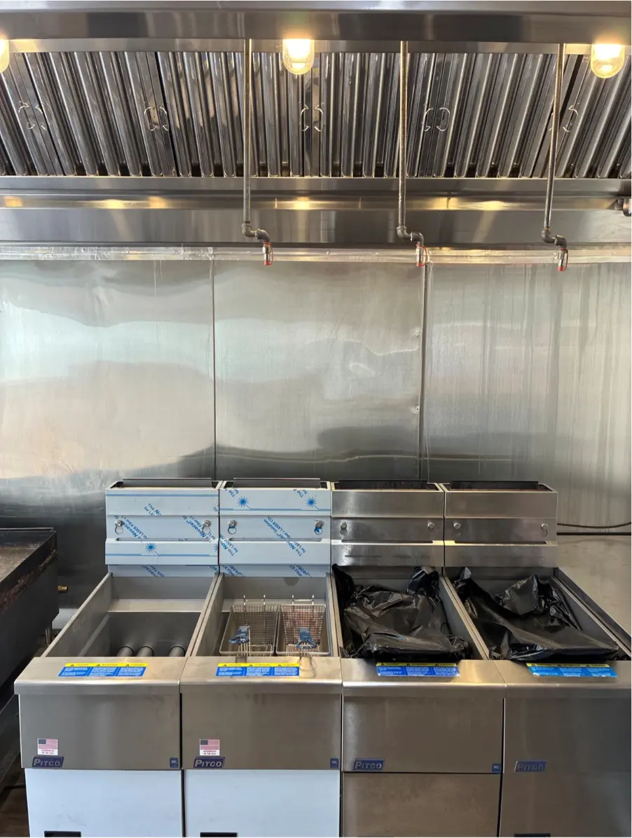 Commercial kitchen exhaust hood with fire suppression nozzles above a row of Pitco deep fryers