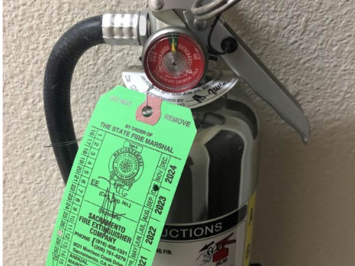Fire extinguisher with a current green State Fire Marshal inspection tag from Sacramento Fire Extinguisher Company