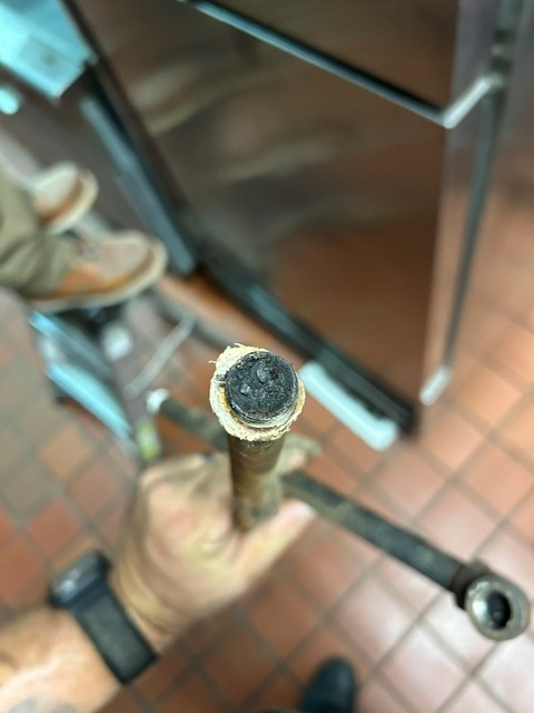 Technician holding a corroded pipe with heavy buildup blocking its opening, found during a fire system service in a commercial kitchen