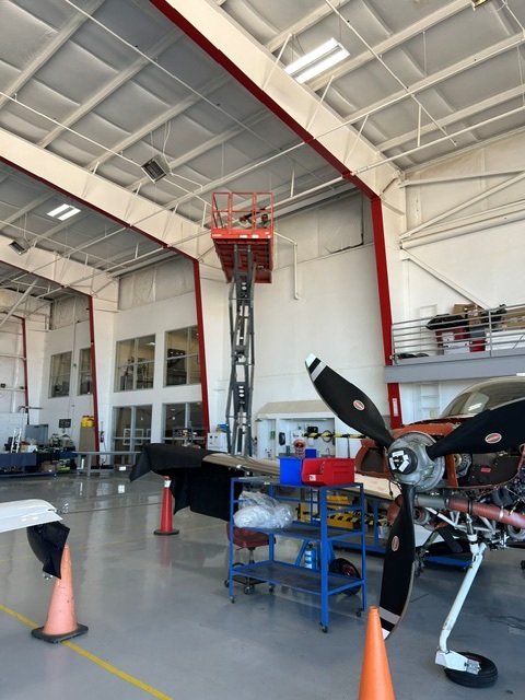 Aircraft hangar with a scissor lift raised to the ceiling for overhead fire protection work at a commercial facility in Sacramento